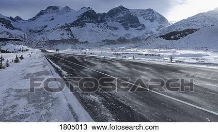 Stock Image - Snowdrift over remote road below snow covered mountains, Columbia Icefield, Alberta, Canada. Fotosearch
