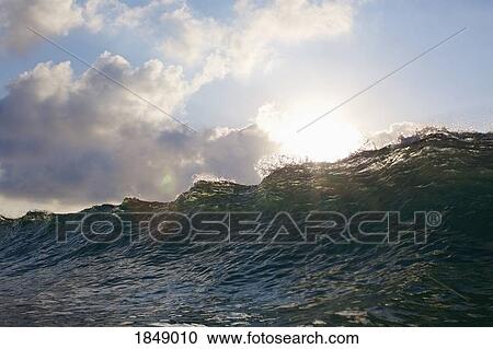 Stock Image - Sun shining over cresting ocean wave. Fotosearch