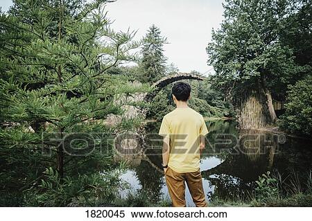 Teenage boy looking at tranquil Rakotzbruecke Devils Bridge, Rakotzbruecke, Brandenburg, Germany View Large Photo Image Stock Photography - Teenage boy looking at tranquil Rakotzbruecke Devils Bridge, Rakotzbruecke, Brandenburg, Germany. Fotosearch