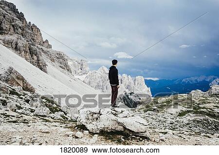 Teenage boy standing on rock overlooking rugged mountains, Drei Zinnen Nature Park, South Tyrol View Large Photo Image Stock Photo - Teenage boy standing on rock overlooking rugged mountains, Drei Zinnen Nature Park, South Tyrol. Fotosearch