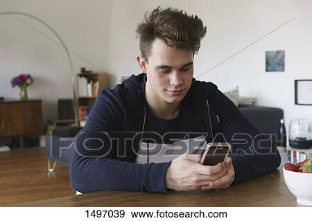 Teenager using smart phone on table at home View Large Photo Image Stock Photo - Teenager using smart phone on table at home. Fotosearch