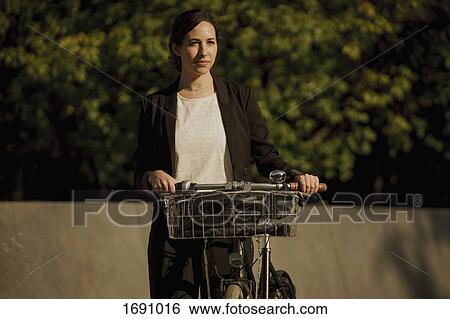 Thoughtful businesswoman standing with bicycle on sunny day View Large Photo Image Stock Photograph - Thoughtful businesswoman standing with bicycle on sunny day. Fotosearch