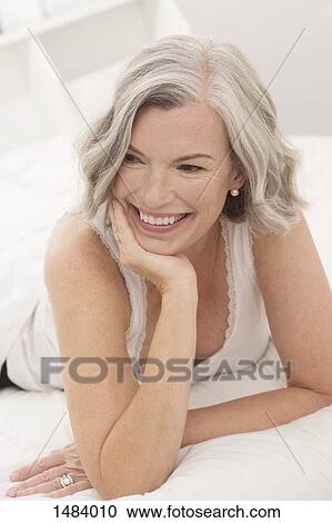 Thoughtful mature woman smiling while lying on bed at home View Large Photo Image Stock Image - Thoughtful mature woman smiling while lying on bed at home. Fotosearch