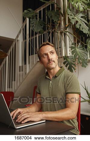 Thoughtful mid adult man looking away while using laptop at table View Large Photo Image Picture - Thoughtful mid adult man looking away while using laptop at table. Fotosearch