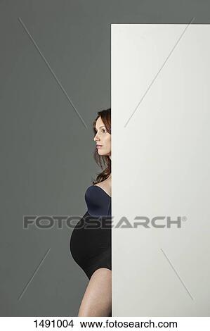Thoughtful pregnant woman standing behind screen against gray background View Large Photo Image Picture - Thoughtful pregnant woman standing behind screen against gray background. Fotosearch