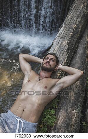 Thoughtful shirtless man lying on logs over waterfall at forest View Large Photo Image Stock Image - Thoughtful shirtless man lying on logs over waterfall at forest. Fotosearch