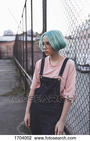 Stock Image - Thoughtful teenage girl standing by fence in city. Fotosearch