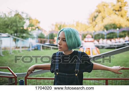 Stock Image - Thoughtful teenage girl standing by railing at amusement park. Fotosearch