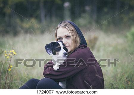 Thoughtful woman embracing dog while sitting on grassy field View Large Photo Image Stock Photo - Thoughtful woman embracing dog while sitting on grassy field. Fotosearch
