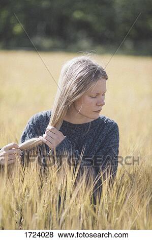Stock Photo - Thoughtful woman holding long hair amidst grass during sunny day. Fotosearch
