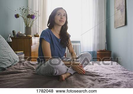 Thoughtful woman sitting on bed View Large Photo Image Stock Photo - Thoughtful woman sitting on bed. Fotosearch