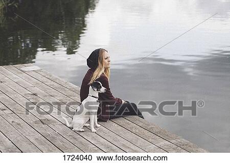 Thoughtful woman sitting with dog on jetty over lake View Large Photo Image Stock Image - Thoughtful woman sitting with dog on jetty over lake. Fotosearch