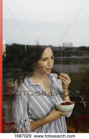 Thoughtful young woman eating red currants while looking through window View Large Photo Image Stock Photo - Thoughtful young woman eating red currants while looking through window. Fotosearch