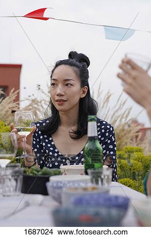 Picture - Thoughtful young woman holding wineglass while sitting at outdoor table during party. Fotosearch