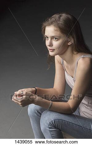 Stock Photography - Thoughtful young woman looking away while sitting against gray background. Fotosearch