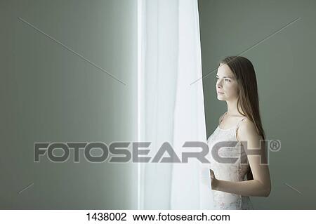 Stock Image - Thoughtful young woman looking through window at home. Fotosearch