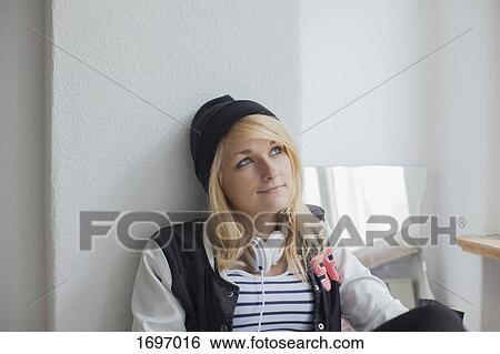 Thoughtful young woman sitting against white wall at home View Large Photo Image Stock Photograph - Thoughtful young woman sitting against white wall at home. Fotosearch