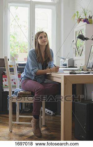 Thoughtful young woman sitting at table in room View Large Photo Image Stock Photo - Thoughtful young woman sitting at table in room. Fotosearch