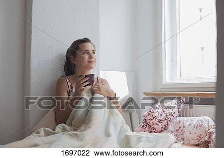 Thoughtful young woman sitting with coffee cup on bed at home View Large Photo Image Stock Image - Thoughtful young woman sitting with coffee cup on bed at home. Fotosearch