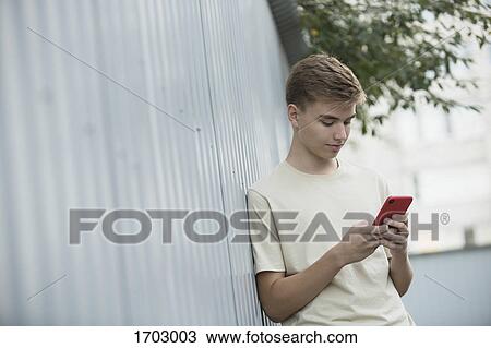 Tilt image of teenage boy using mobile phone while leaning on metallic wall View Large Photo Image Stock Image - Tilt image of teenage boy using mobile phone while leaning on metallic wall. Fotosearch