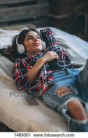 Trendy young woman listening music while lying on bed at home View Large Photo Image Stock Image - Trendy young woman listening music while lying on bed at home. Fotosearch