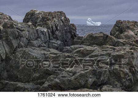 View of iceberg in sea through rocks on shore, Fogo Island, Newfoundland, Canada View Large Photo Image Picture - View of iceberg in sea through rocks on shore, Fogo Island, Newfoundland, Canada. Fotosearch