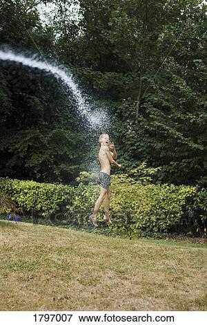 Stock Photo - Water spraying boy in swim trunks in backyard. Fotosearch