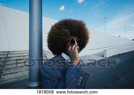Stock Photo - Well-dressed young man with afro smoking cigarette on urban sidewalk. Fotosearch