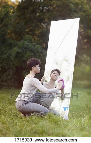 Woman cleaning mirror while crouching on grassy field at park View Large Photo Image Stock Photo - Woman cleaning mirror while crouching on grassy field at park. Fotosearch