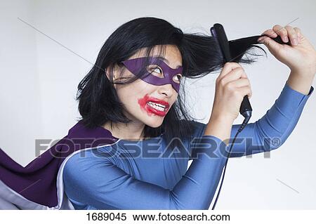 Stock Photography - Woman dressed as superhero straightening hair against gray background. Fotosearch