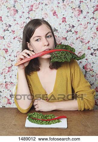 Stock Image - Woman eating chard while sitting at table. Fotosearch