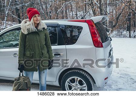 Woman holding backpack while standing by car on field View Large Photo Image Stock Photo - Woman holding backpack while standing by car on field. Fotosearch