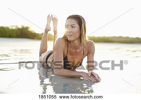 Stock Photography - Woman in bikini laying in sunny ocean surf. Fotosearch