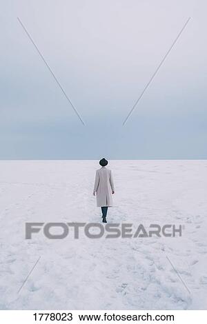 Stock Image - Woman in coat and hat walking in snow covered landscape. Fotosearch