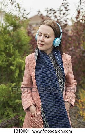 Woman in scarf and coat listening to music with headphones View Large Photo Image Stock Image - Woman in scarf and coat listening to music with headphones. Fotosearch