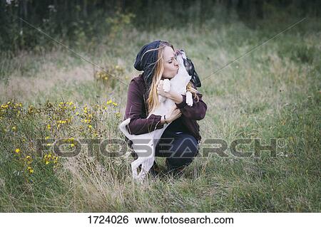 Woman kissing dog while crouching in grassy field View Large Photo Image Stock Photograph - Woman kissing dog while crouching in grassy field. Fotosearch