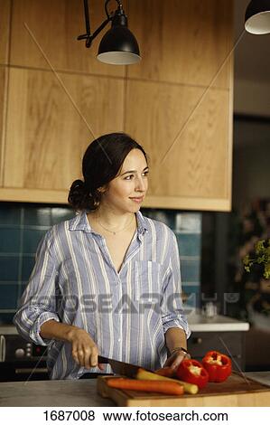 Woman looking away while chopping carrot at kitchen island View Large Photo Image Stock Photo - Woman looking away while chopping carrot at kitchen island. Fotosearch