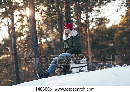 Stock Photography - Woman looking away while sitting on log during winter. Fotosearch