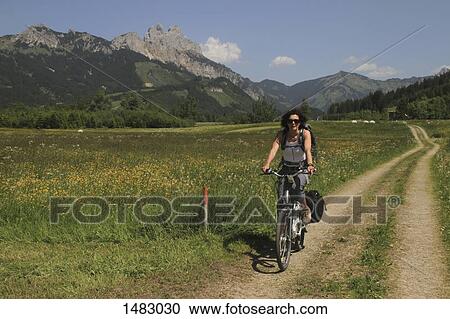 Woman riding bicycle on road by grassy field against mountains View Large Photo Image Stock Image - Woman riding bicycle on road by grassy field against mountains. Fotosearch