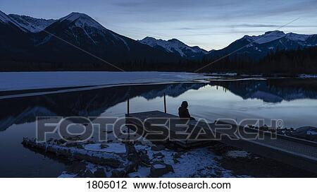 Woman sitting on tranquil winter lake dock with mountain view at night, Banff, Alberta, Canada View Large Photo Image Stock Image - Woman sitting on tranquil winter lake dock with mountain view at night, Banff, Alberta, Canada. Fotosearch