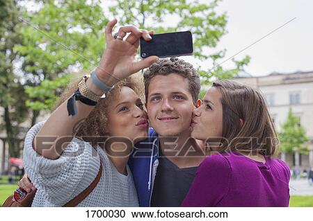 Woman taking selfie with female friend while kissing young male View Large Photo Image Stock Image - Woman taking selfie with female friend while kissing young male. Fotosearch