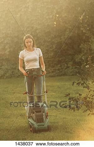 Stock Photo - Woman trimming grass with lawn mower at yard. Fotosearch