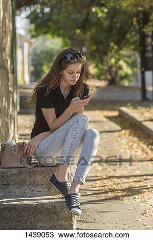 Stock Image - Woman using smart phone while sitting on steps outdoors. Fotosearch