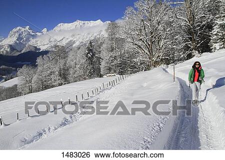 Stock Photograph - Woman walking on snow covered field against mountains. Fotosearch