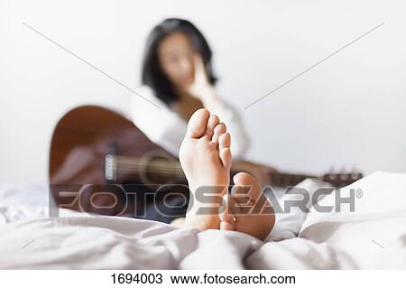 Woman with bare feet holding guitar while resting on bed at home View Large Photo Image Stock Image - Woman with bare feet holding guitar while resting on bed at home. Fotosearch