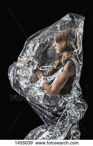 Stock Photo - Woman wrapped in plastic standing against black background. Fotosearch
