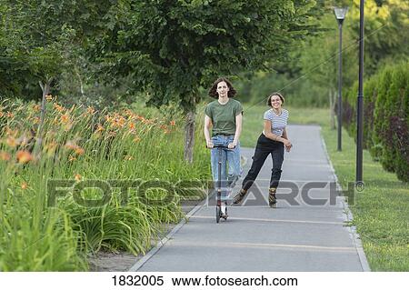 Stock Photography - Women rollerblading and riding push scooter on park footpath. Fotosearch