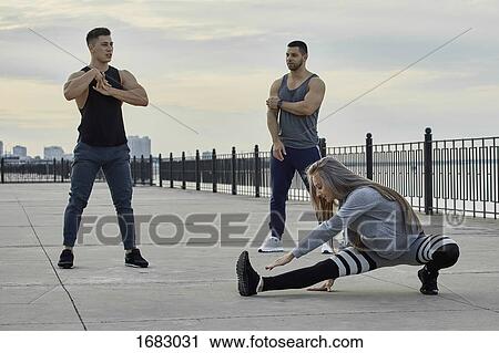Stock Image - Young athletes stretching on promenade during sunset. Fotosearch
