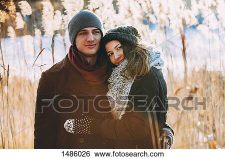 Young couple embracing while standing on field View Large Photo Image Stock Photograph - Young couple embracing while standing on field. Fotosearch