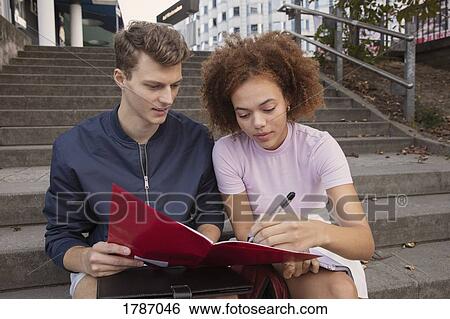 Stock Photograph - Young couple filling out paperwork on urban steps. Fotosearch